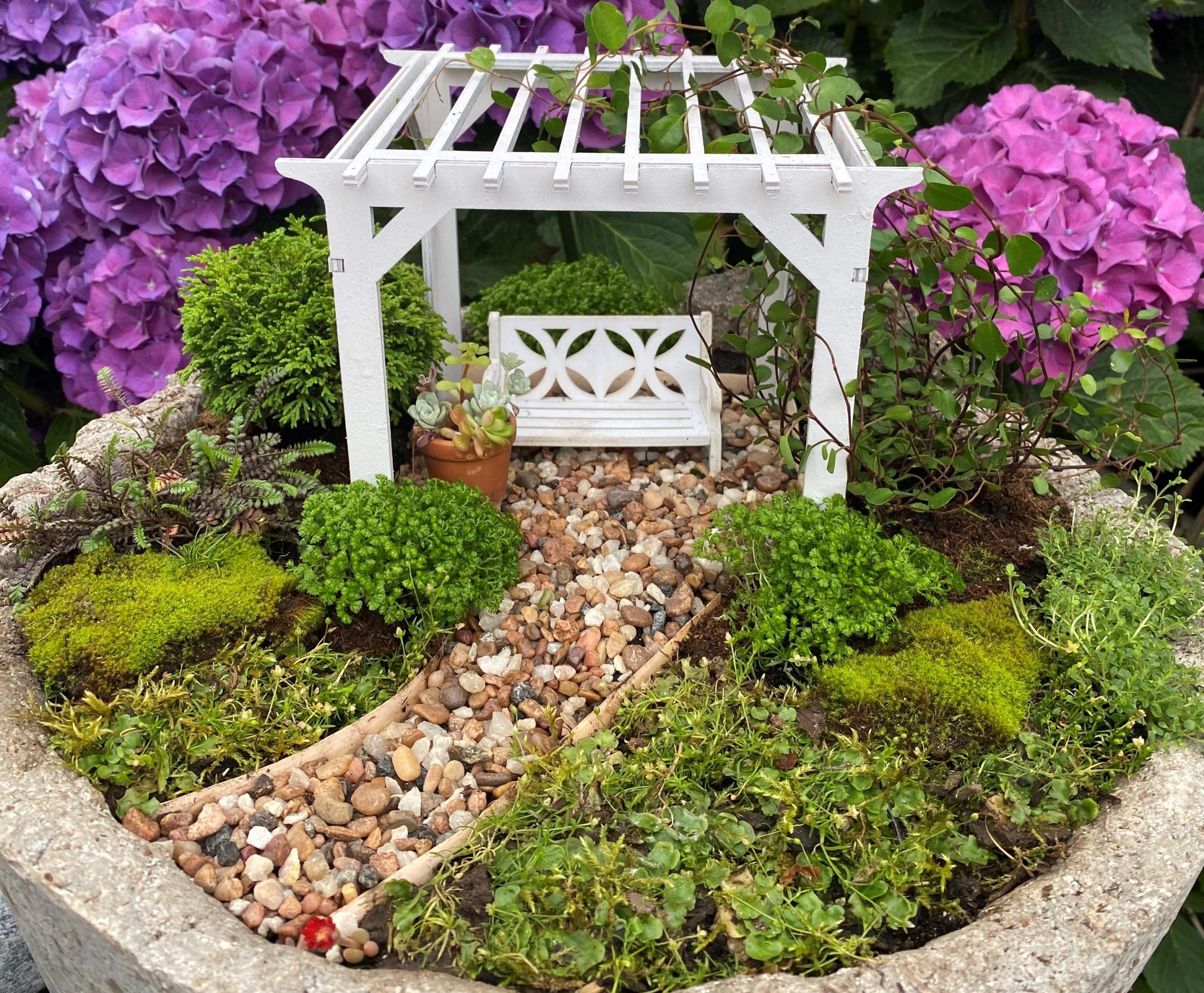 Miniature landscape with an arbor, swing and pathway in front of blooming hydrangeas.